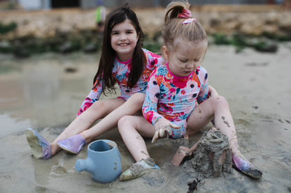 Blue plastic watering can with spade, held while playing in sand