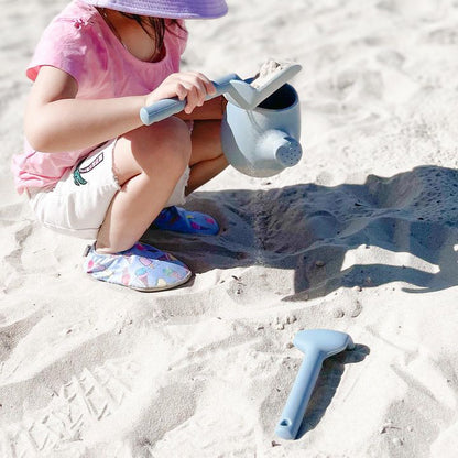 Blue plastic watering can with spade and rake accessories in sand