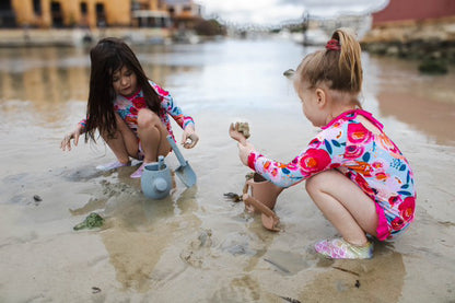 Blue plastic watering can with spade, used by children in shallow water