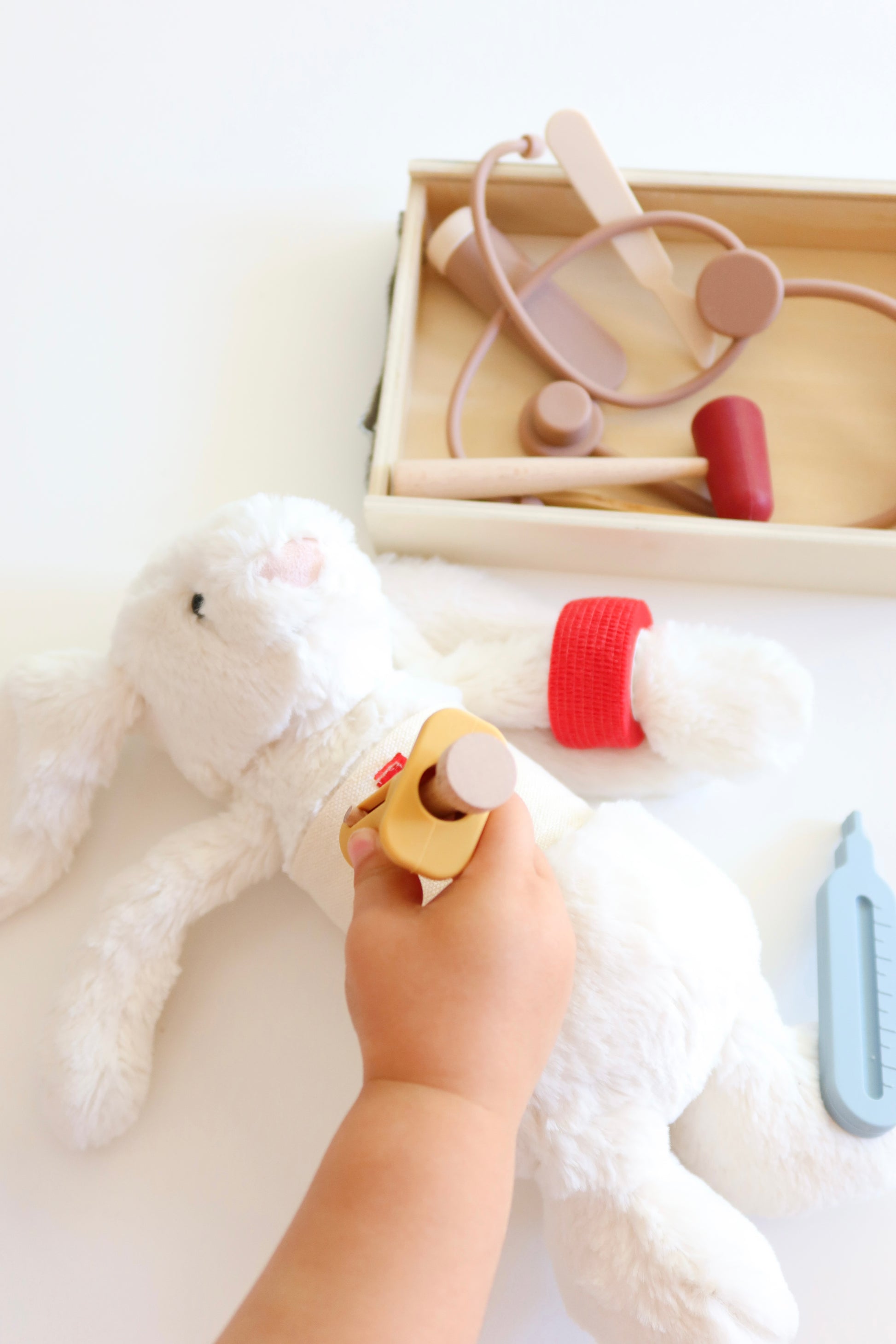 Child's hand holding a silicone toy near a white teddy bear and other pieces from doctors set nearby