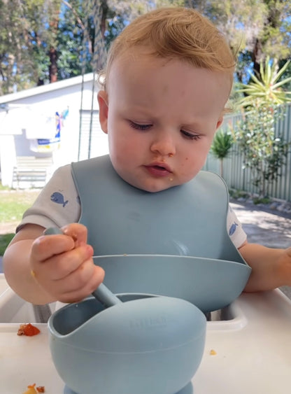 Blue suction bowl with spoon on a high chair, child eating