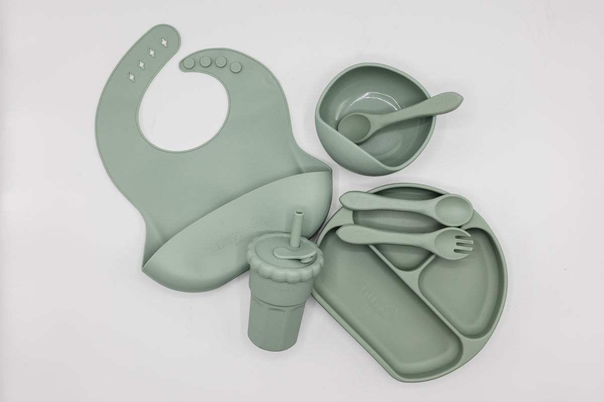 Sage silicone feeding set flat lay, including bib, divided plate, bowl, and utensils