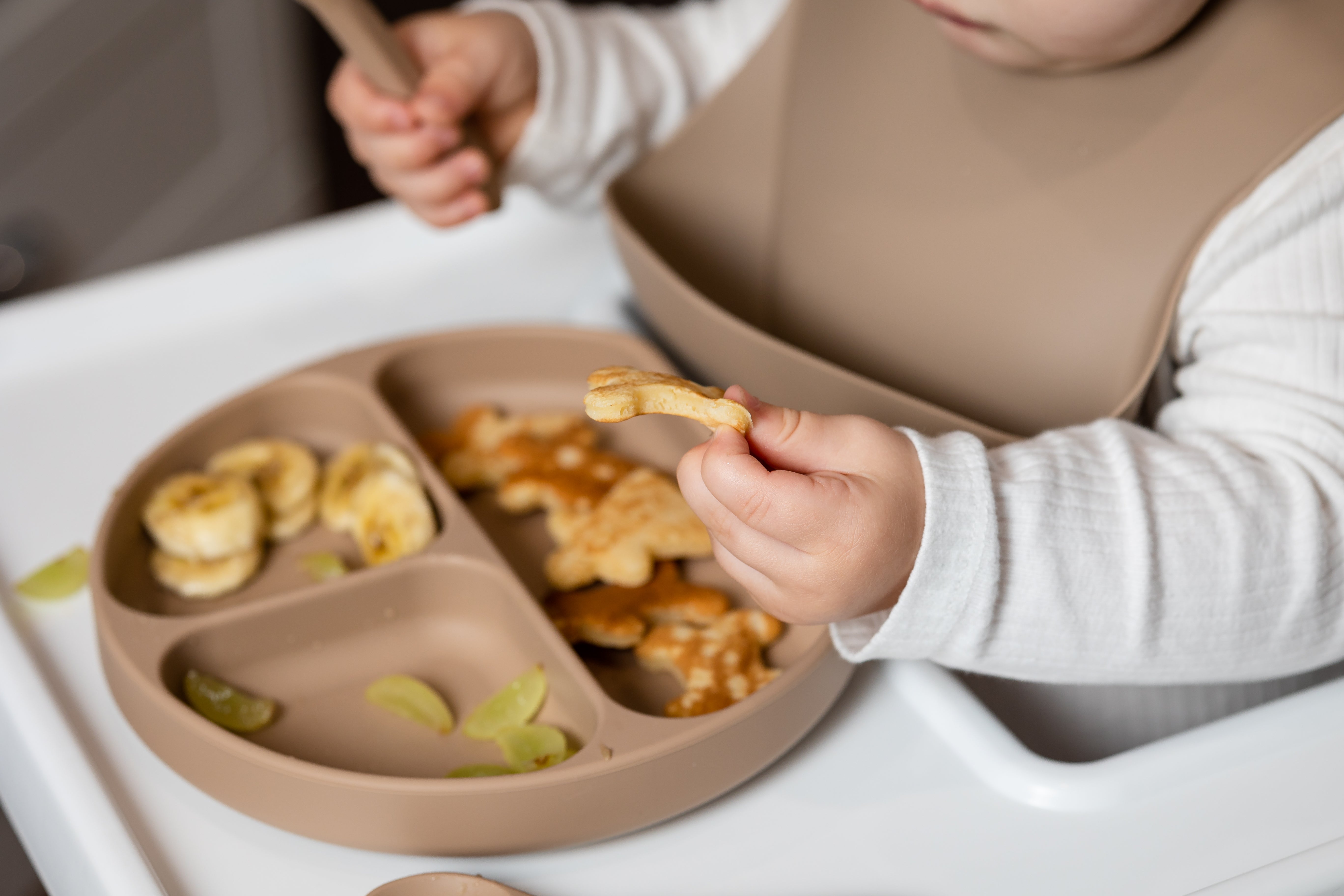 Child eating from a silicone dinner plate from Lil Finch Boutique on high chair