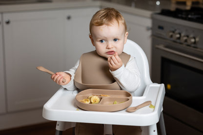 Beige baby feeding set on a high chair, with divided plate and spoon for eating