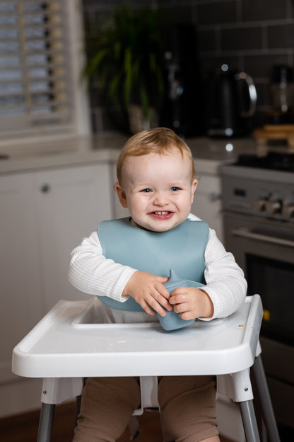Sage green silicone bucket bib on toddler in high chair