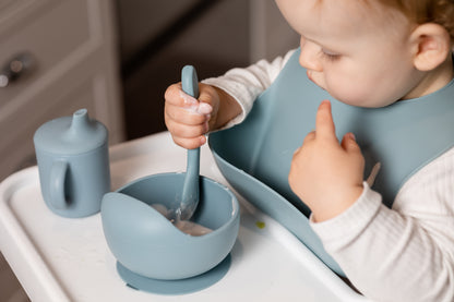 Dusty blue silicone bucket bib on toddler with open-back pocket