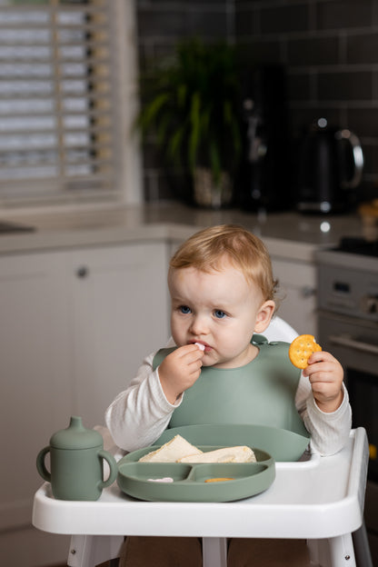 Sage green silicone bucket bib with front pocket on toddler