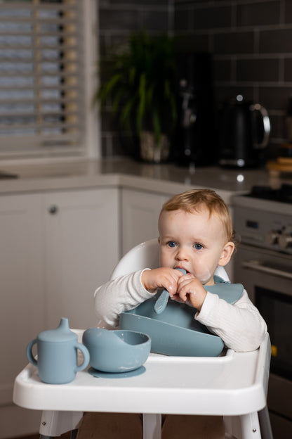Blue suction bowl set with spoon on a high chair, child holding food