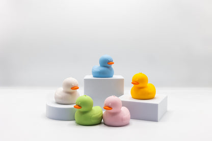5 squeeze duck bath toys grouped on white steps: blue, yellow, green, pink