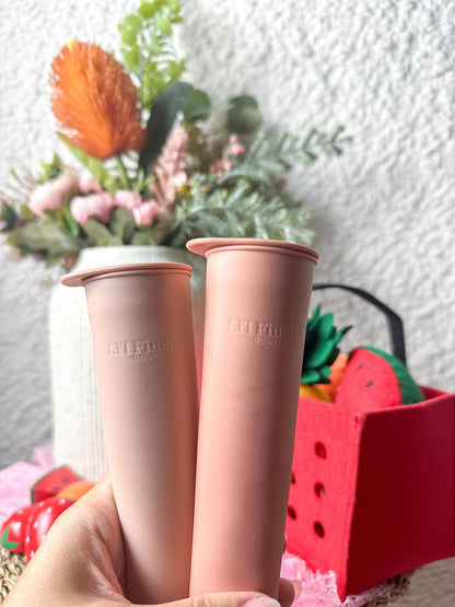 Popsicle mold tubes in pink and tan, held upright