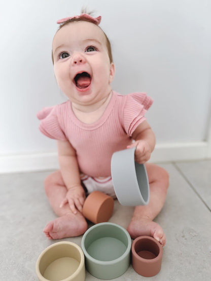 Baby holding stacking cups with three pastel bowls in mint, gray, and peach