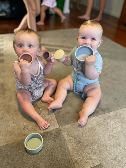 Two babies playing with pastel stacking cups held in their hands and on the floor