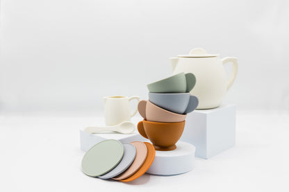 Tea party set with white teapot, colored nesting cups, and stacked saucers