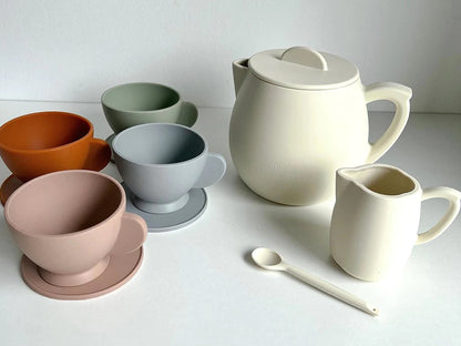 Tea party set with cream teapot, cups, and stacked colored bowls with spoon