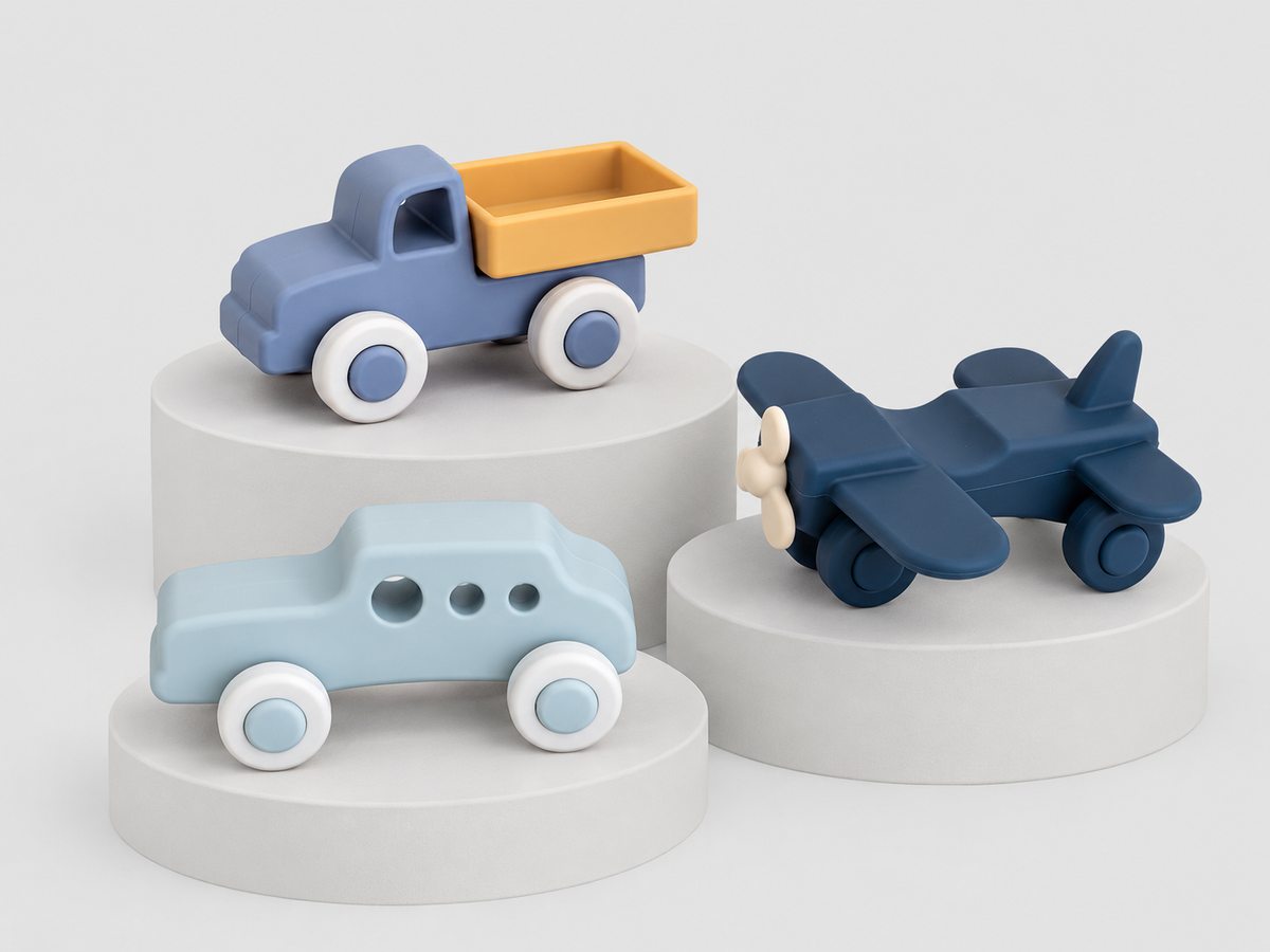 Three silicone toy vehicles for toddlers: a blue pickup truck with a yellow bed, a light blue car, a dark blue airplane, and a small blue vehicle with a yellow cargo bed.