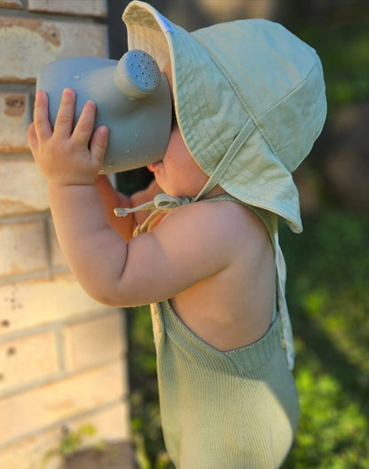Kids watering can toy with light blue scoop; child holding it by brick wall